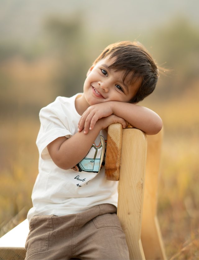 A smiling boy resting on a wooden chair in golden light